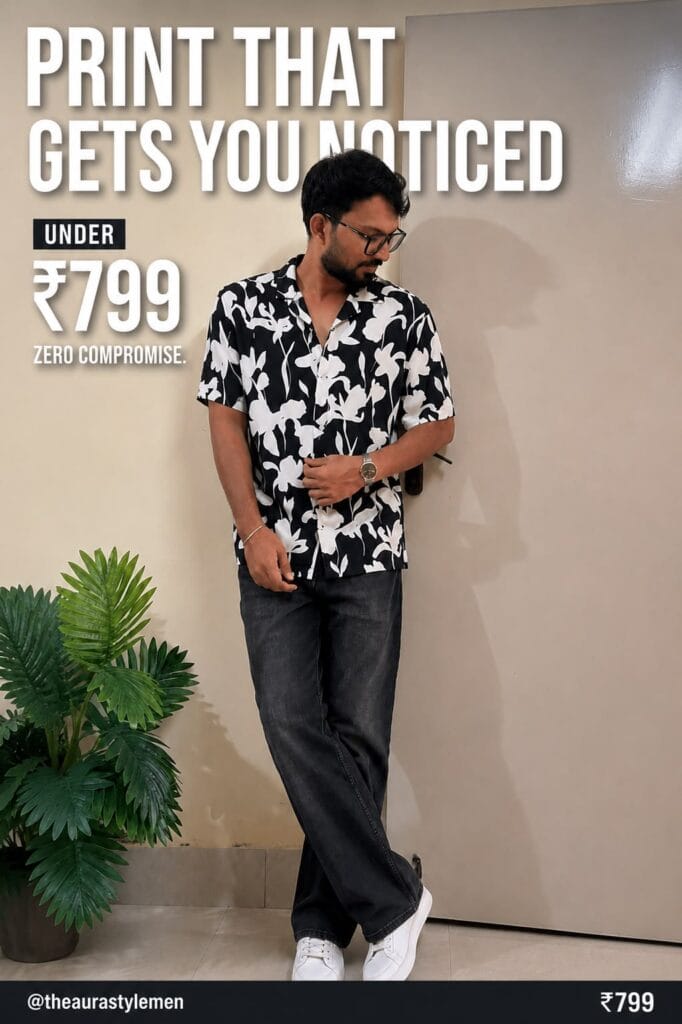 Young Indian man wearing black floral Cuban collar shirt with dark jeans and white sneakers, standing indoors.