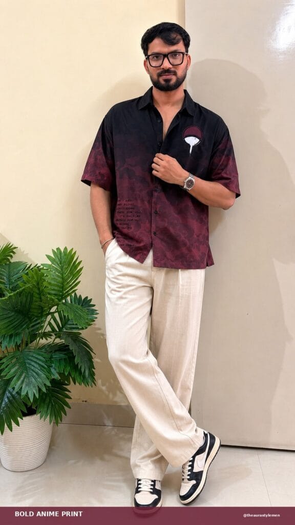 Man wearing a relaxed black and maroon anime print shirt with cream wide-leg trousers and sneakers for a trendy college outfit.