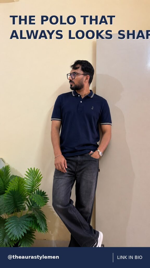 Man wearing a navy tipped polo, charcoal jeans and white sneakers indoors.