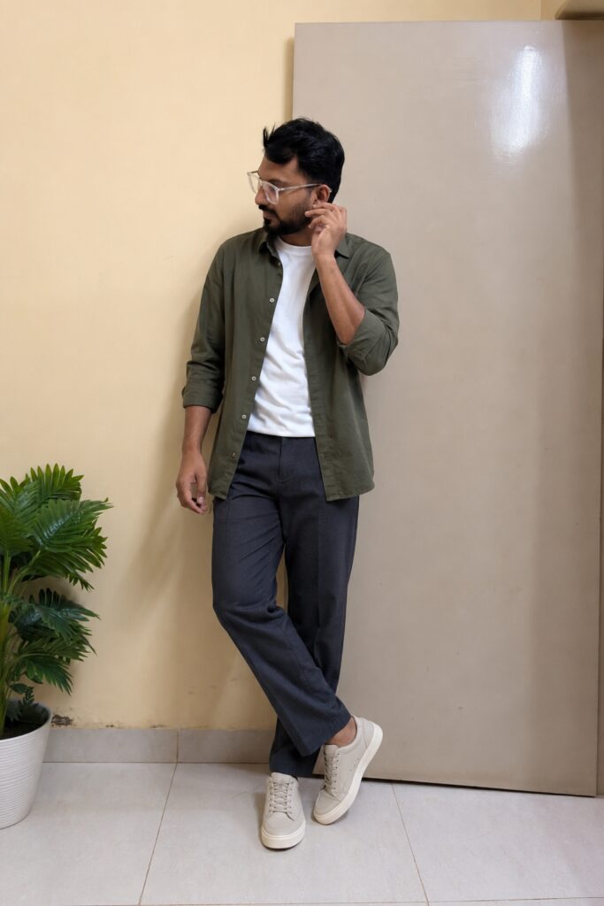 Indian man wearing an olive lightweight overshirt, white T-shirt, charcoal trousers and beige sneakers for the monsoon