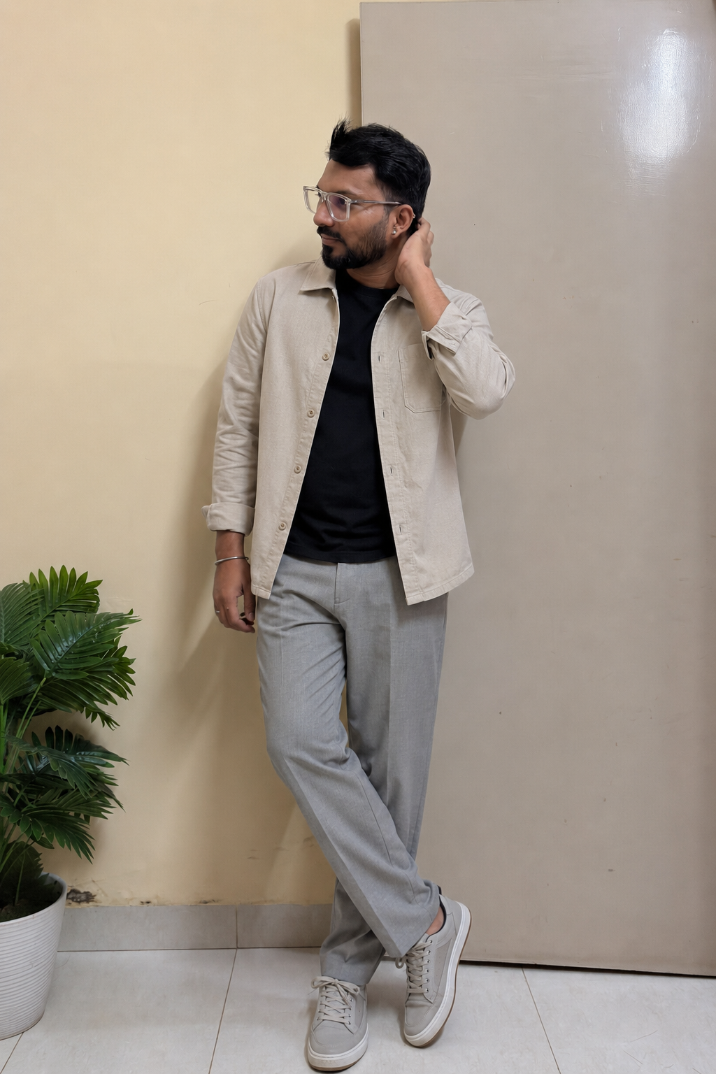 Indian man wearing a beige lightweight shacket, black T-shirt and grey trousers for a rainy evening