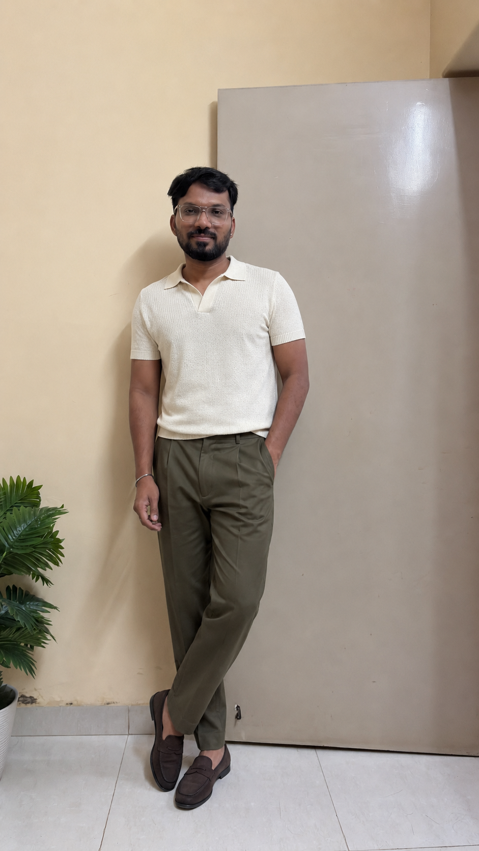 Indian man wearing a cream knitted polo, olive pleated trousers and tan loafers in monsoon