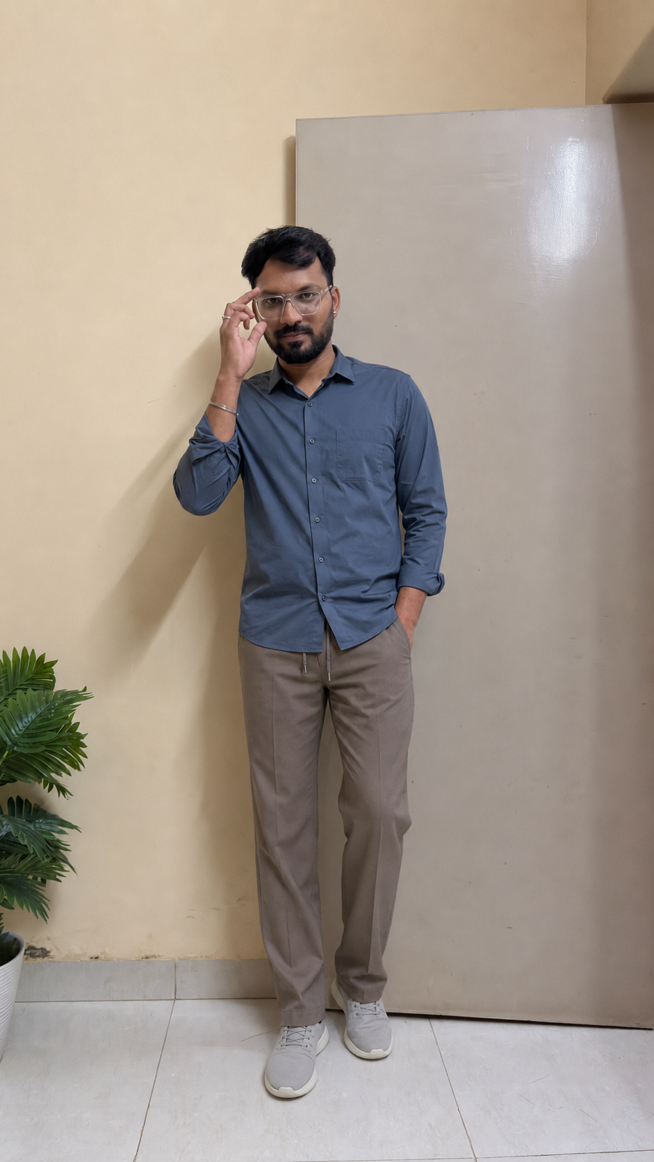 Indian man wearing a slate-blue travel shirt, taupe drawstring trousers and grey trainers for monsoon travel